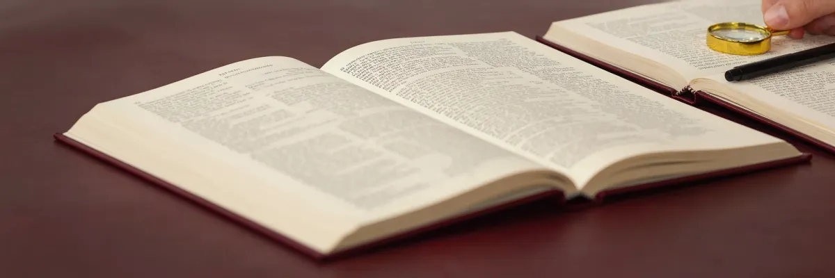 A hand holding a magnifying glass over an open reference book.