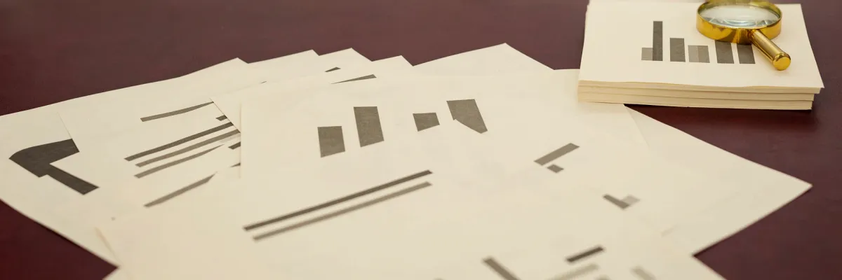 Printed pages of abstract bar-chart graphics beside a magnifying glass.