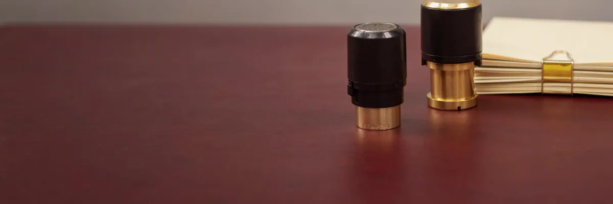 A modern desk stamp beside a stack of documents fastened with a paperclip.